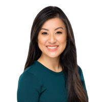 A professional headshot of a person wearing a teal long-sleeve top, photographed against a light gray background.