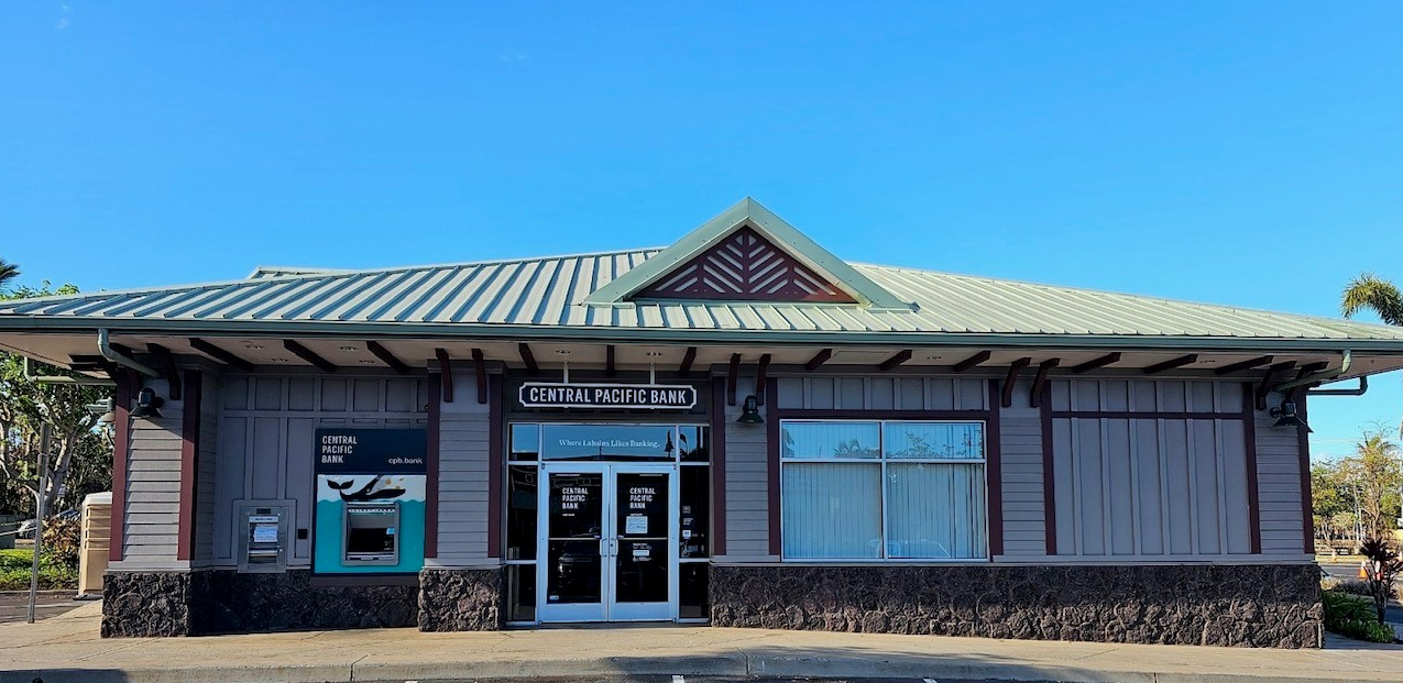 A Central Pacific Bank branch with an exterior ATM is shown under a clear blue sky. The single-story building features large windows, stone accents, and prominent Central Pacific Bank signage above the entrance.
