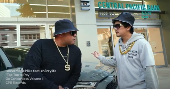 Two people wearing bucket hats, sunglasses, and oversized gold chains stand in front of a Central Pacific Bank branch and a parked vehicle. On-screen text references the song “Tap Topay” and “CPB Records Volume II,” suggesting a promotional music video or marketing campaign.
