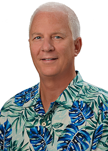A professional headshot of a person with short white hair wearing a green aloha shirt with blue tropical leaf patterns, photographed against a light gray background.