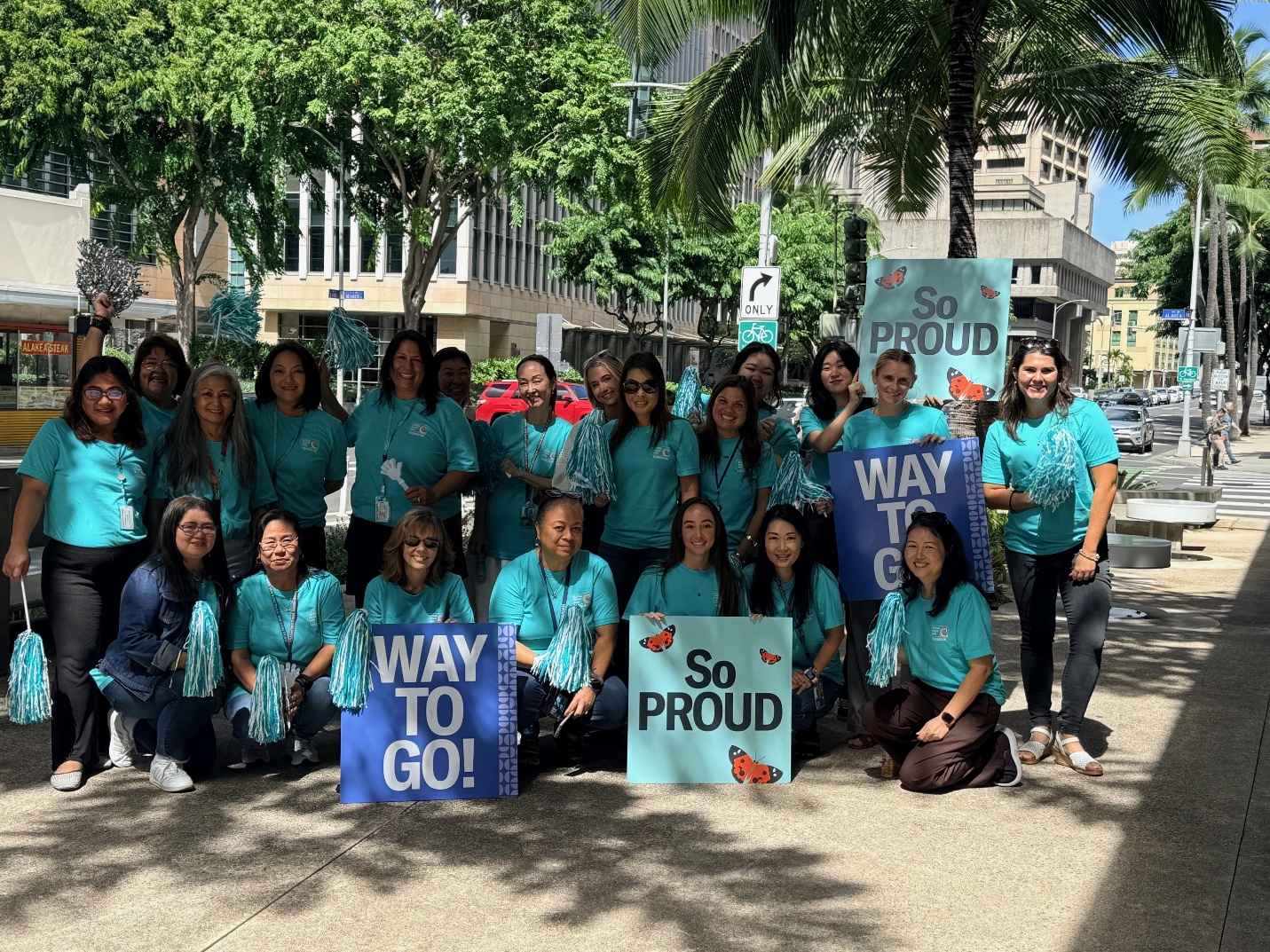 Central Pacific Bank Foundation volunteers gather outdoors with encouragement signs and pom-poms during a community event raising awareness about domestic violence prevention.