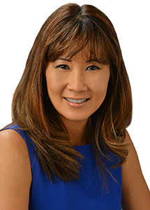 A professional headshot of a person wearing a royal blue sleeveless top, photographed against a light gray background.