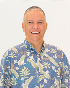 A professional headshot of a person wearing a blue floral Hawaiian shirt, photographed against a plain white background.