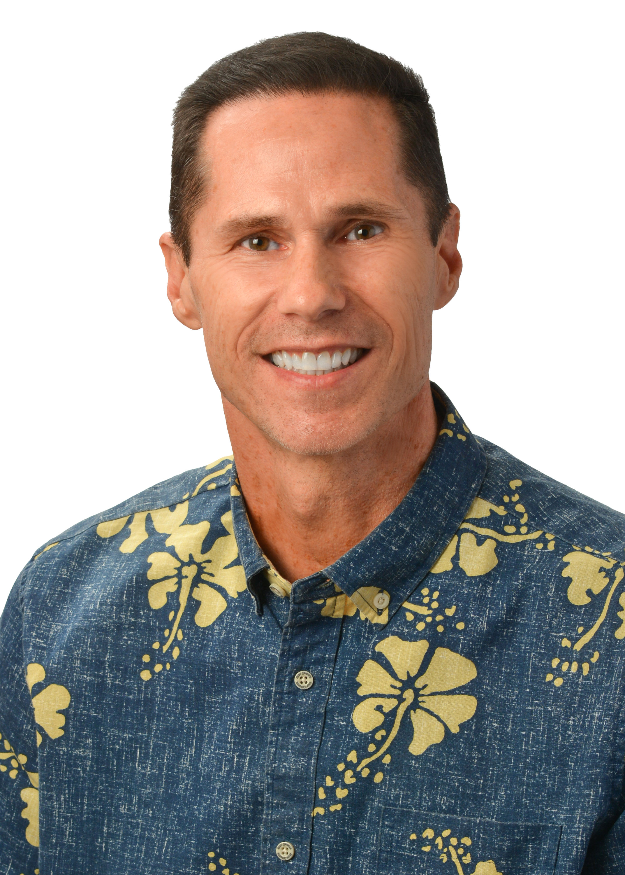 A professional headshot of a person wearing a blue aloha shirt with a yellow hibiscus floral pattern, photographed against a light gray background.