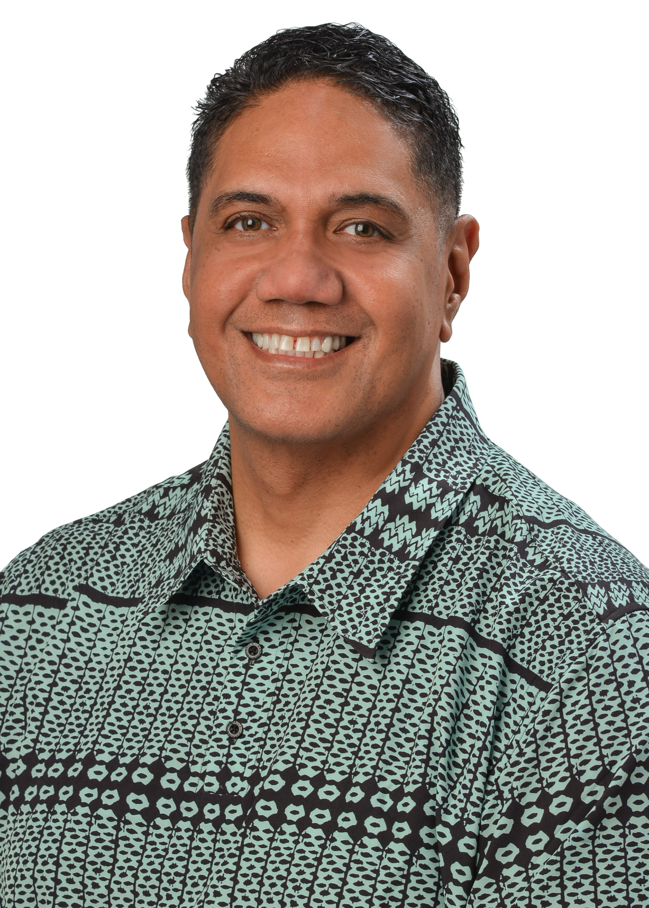 A professional headshot of a person wearing a teal patterned aloha shirt, photographed against a light gray background.