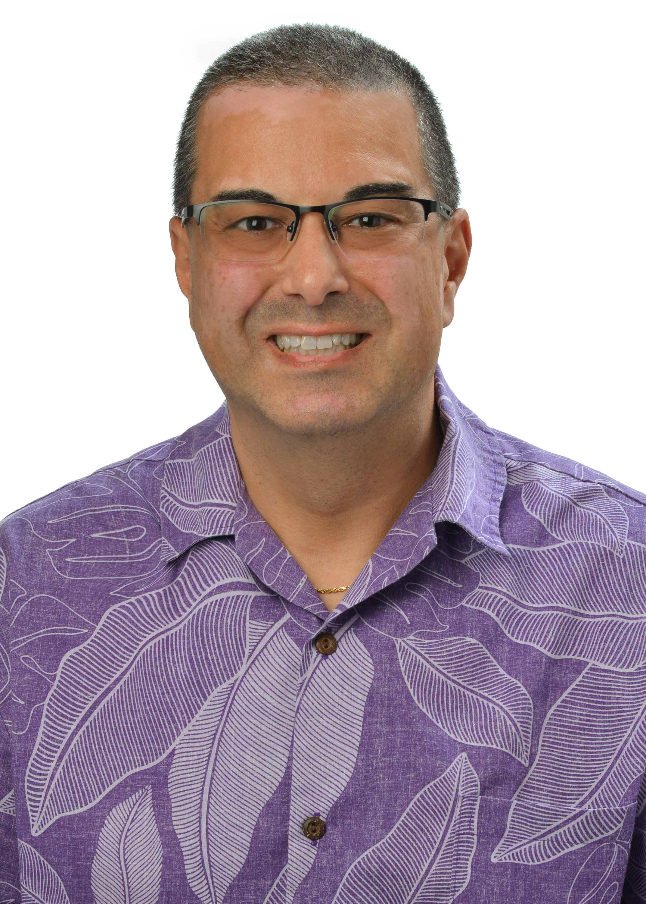 A professional headshot of a person wearing glasses and a purple aloha shirt with a leaf pattern, photographed against a light gray background.