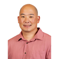 A professional headshot of a person with a shaved head wearing a salmon-colored collared shirt, photographed against a light gray background.
